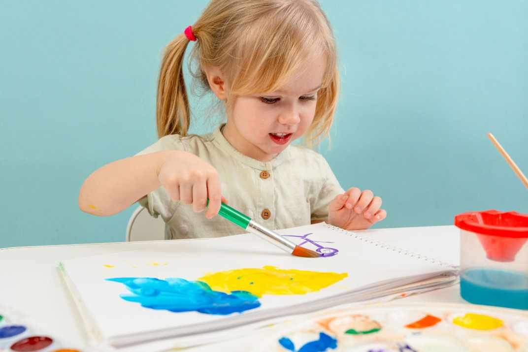 dítě maluje obrázek barvami a pastelkami u stolu